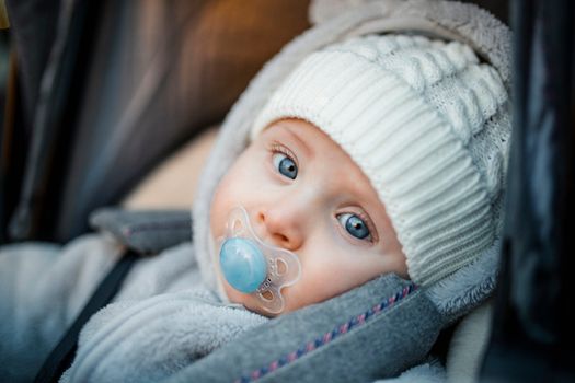Little baby boy sitting in his stroller wearing warm clothing.