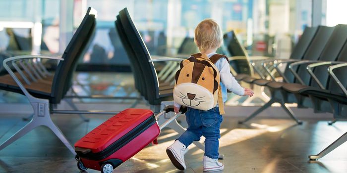 Kid travelling through the airport with suitcase and toys